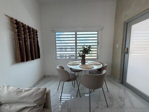 A dining area with a round table, four chairs, a potted plant, and a wall-mounted decorative piece.