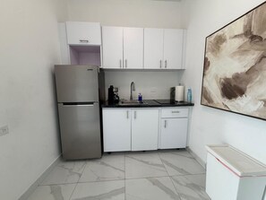 A compact kitchen with white cabinets, a stainless steel refrigerator, a sink, and a countertop.