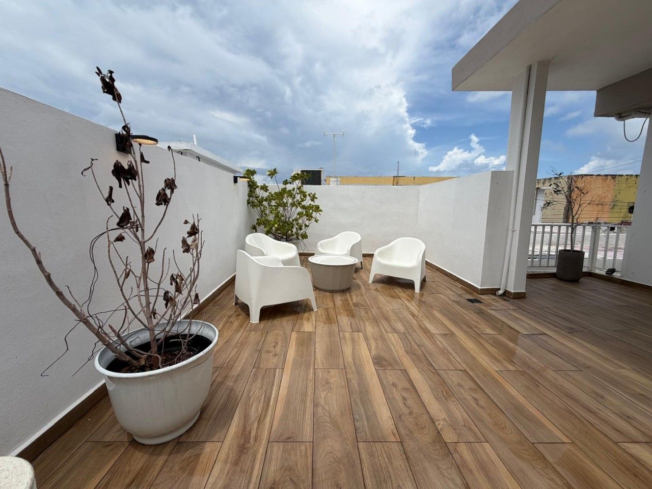 Eine Dachterrasse mit Holzboden, weißen Stühlen und einem Blumentopf.