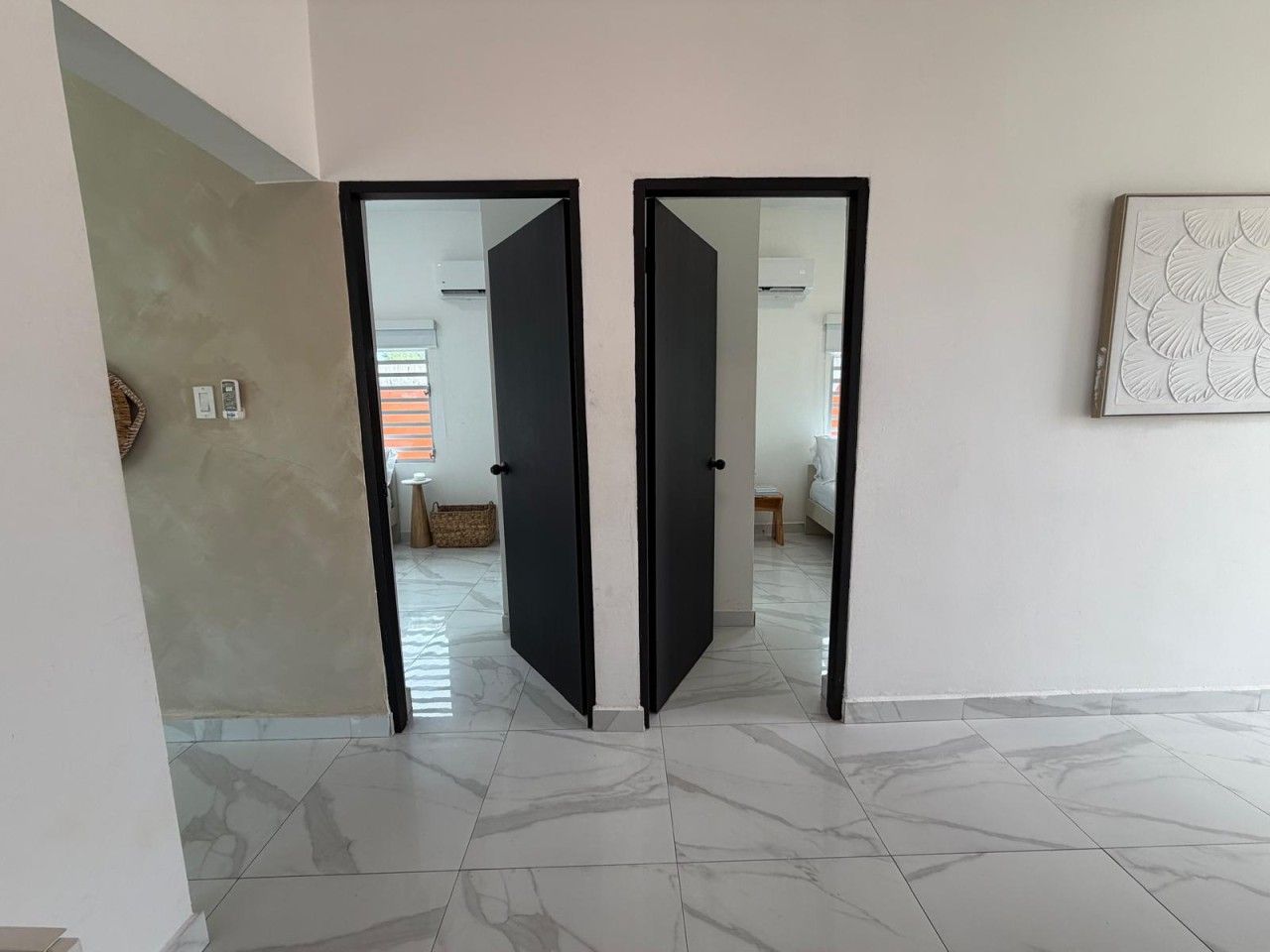 A hallway with a mirrored wall, a tiled floor, and a door leading to another room.