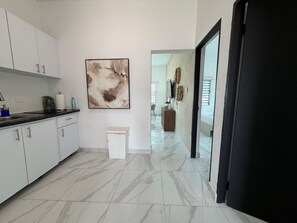 A modern kitchen with white cabinets, a marble floor, and a large abstract painting on the wall.