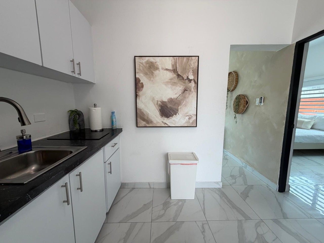 A modern kitchen with a marble countertop, a sink, cabinets, and a trash bin.