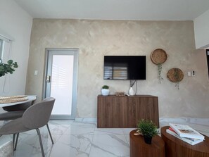 Un salon moderne doté d’un téléviseur à écran plat, d’un meuble en bois et d’un coin repas avec une table et des chaises.