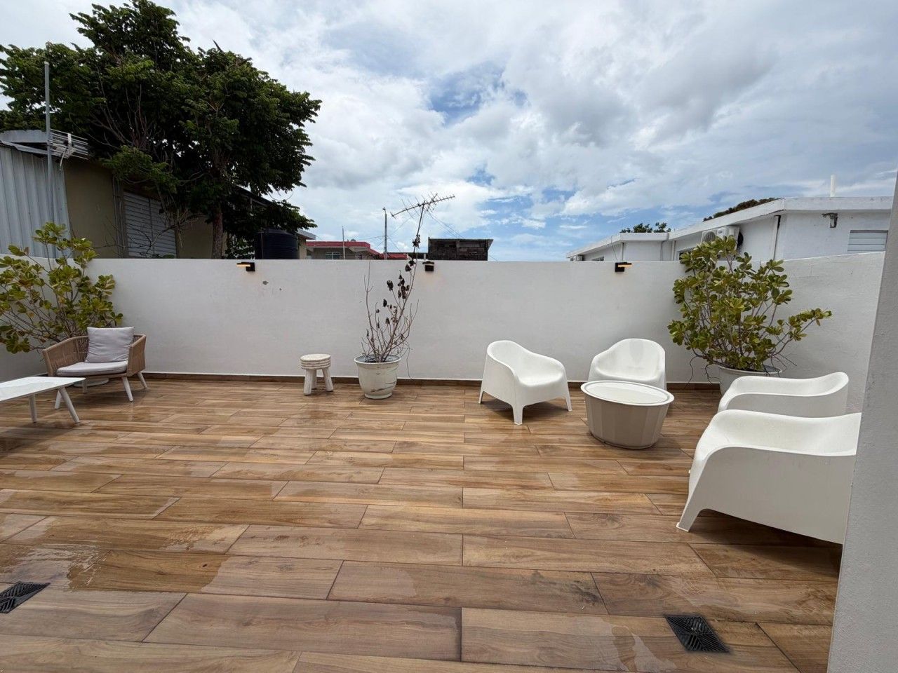 Une terrasse extérieure avec un plancher en bois, des chaises blanches et des plantes en pot.