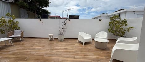 An outdoor patio with wooden flooring, white chairs, and potted plants.