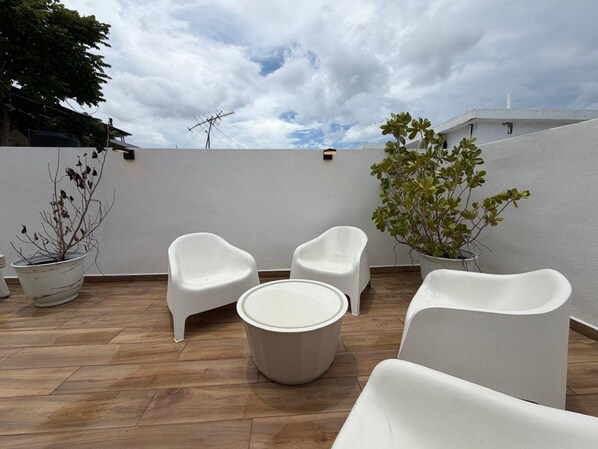 An outdoor seating area with white chairs and a round table, surrounded by potted plants.