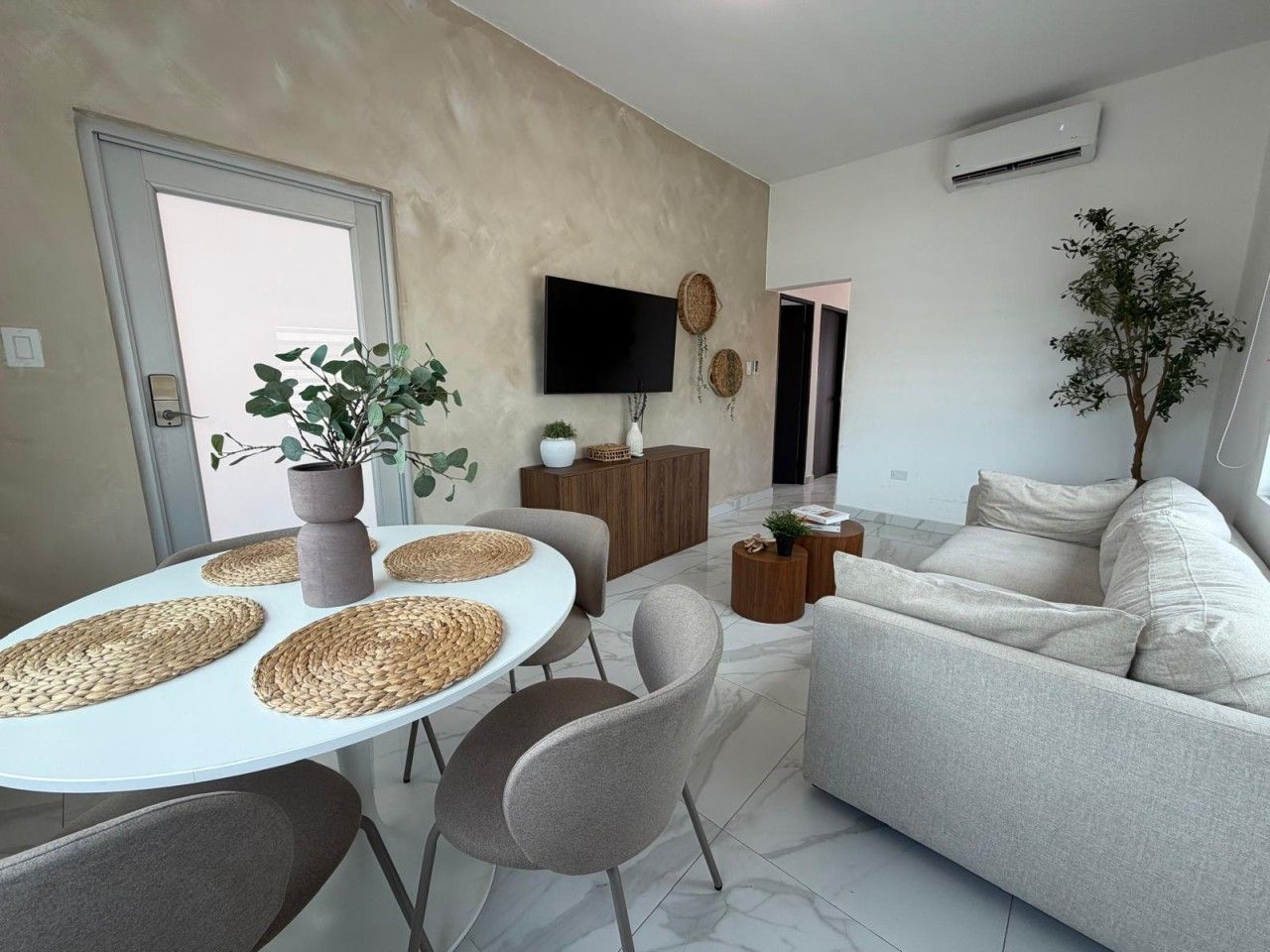 Ein modernes Wohnzimmer mit einer Couch, einem Esstisch mit Unterlagen, einem Fernseher und einer Topfpflanze.