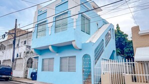 Un bâtiment à deux étages avec une façade bleue, une clôture blanche et un escalier menant à l’étage supérieur.