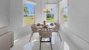 A modern dining area with a round table and wicker chairs, large windows with views of a green landscape, and a ceiling light fixture. - Cozy Beach Front Apt @ Palmas del Mar w/ 2 Pools (Palmas del Mar)
