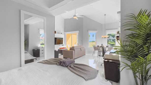 A modern bedroom with a large bed, a desk, and a view of the outdoors. - Cozy Beach Front Apt @ Palmas del Mar w/ 2 Pools (Palmas del Mar)