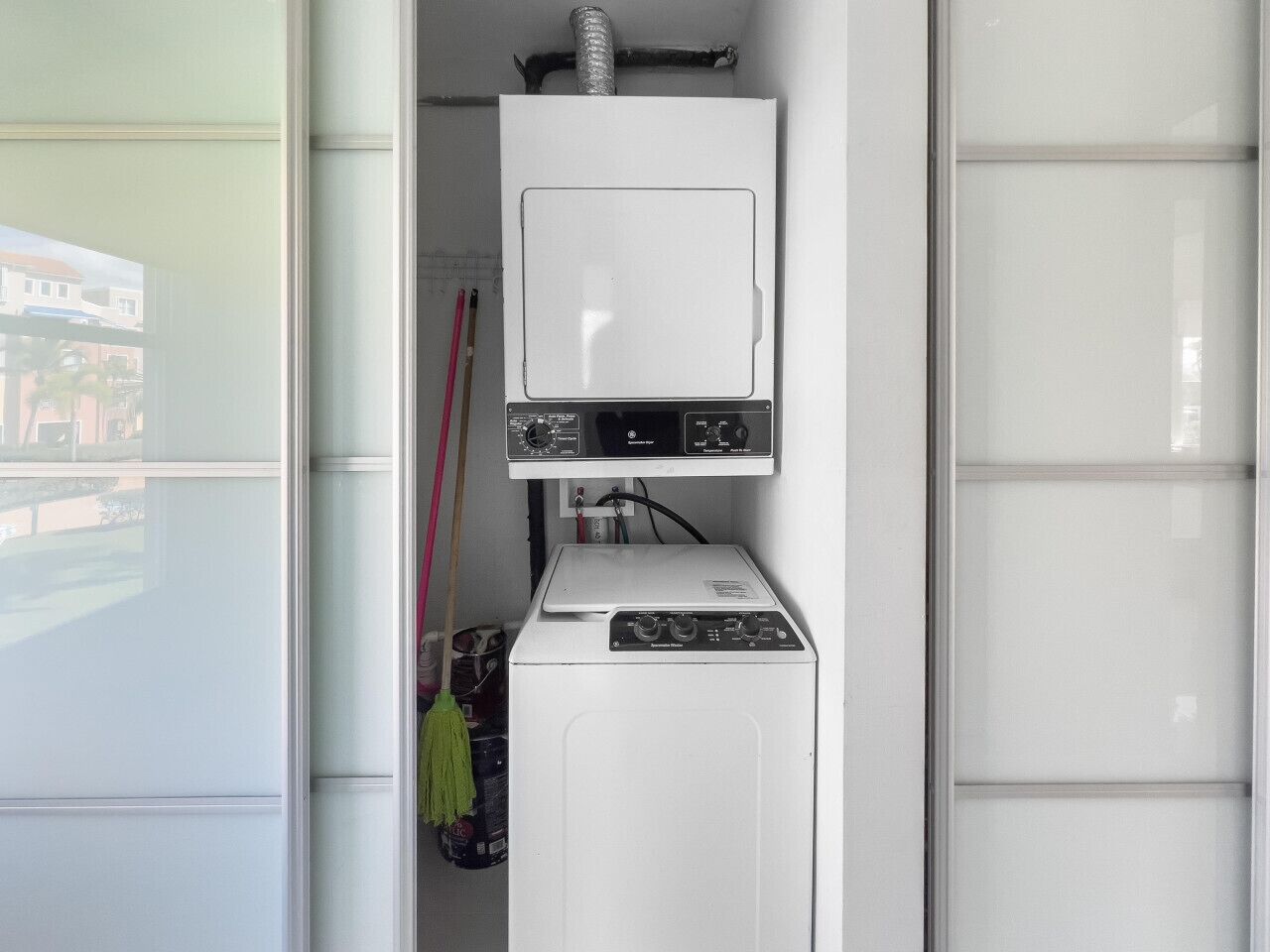 Une petite buanderie équipée d’un lave-linge et d’un sèche-linge à chargement frontal, d’une petite fenêtre et d’une serpillière appuyée contre le mur.