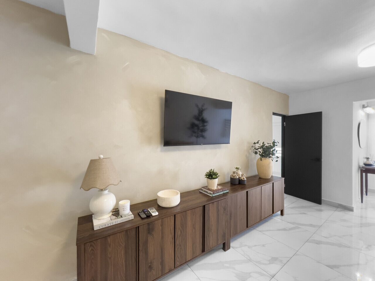 A modern hallway with a wooden console table, a mounted television, and a door leading to another room.