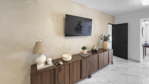A modern hallway with a wooden console table, a mounted television, and a door leading to another room.