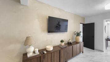 A modern hallway with a wooden console table, a mounted television, and a door leading to another room.
