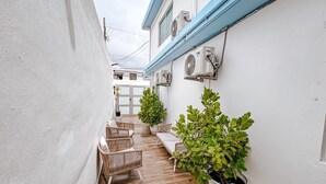 A narrow outdoor patio with wicker furniture and potted plants.