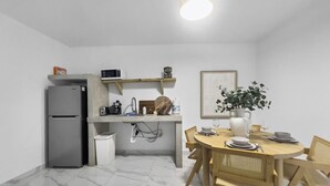 A compact kitchen with a refrigerator, microwave, and sink. There's a dining table with chairs and a potted plant.