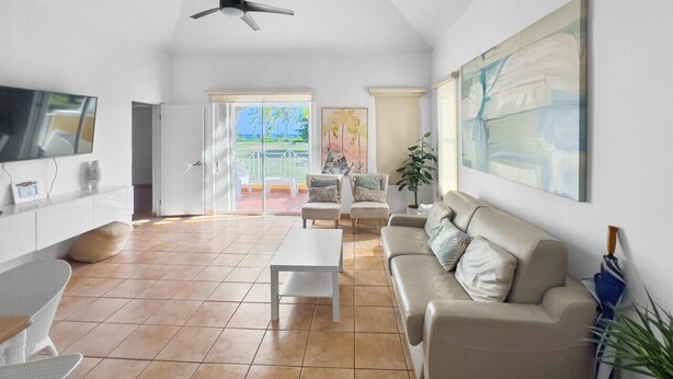 A spacious living room with a large TV, a ceiling fan, a sofa, and a coffee table. - Oasis Beach Apt in Palmas del Mar w/ Pool & Views (Palmas del Mar)