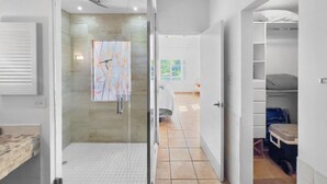A modern bathroom with a glass shower enclosure, a tiled floor, and a visible artwork on the wall. - Oasis Beach Apt in Palmas del Mar w/ Pool & Views (Palmas del Mar)