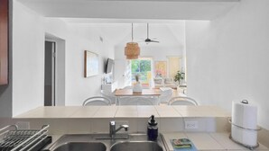 A modern kitchen with a double sink, a dining area with a table and chairs, and a hanging light fixture. - Oasis Beach Apt in Palmas del Mar w/ Pool & Views (Palmas del Mar)