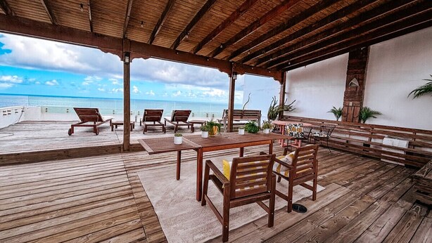 Eine Holzterrasse mit Tisch und Stühlen mit Blick auf einen Strand.