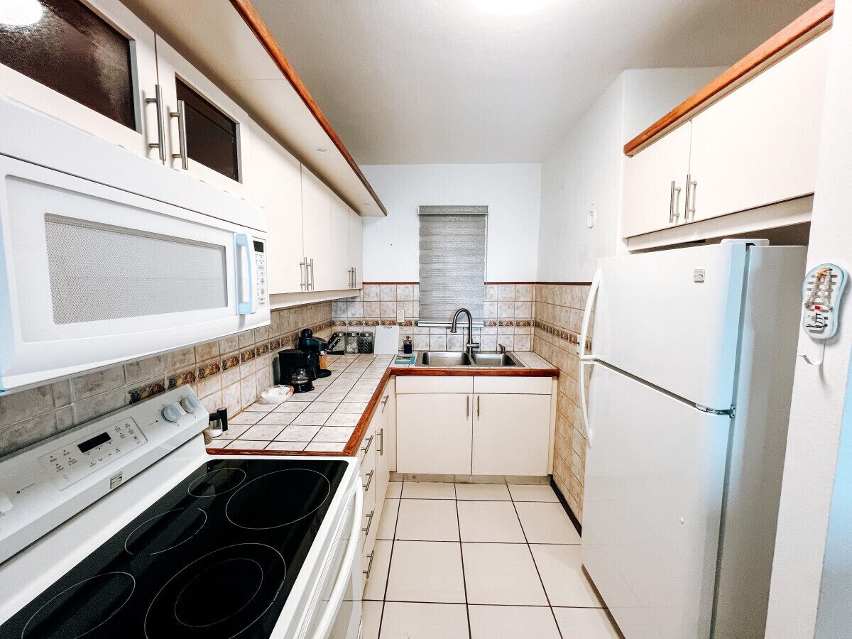 A compact kitchen with white cabinets, a microwave, a stove, a sink, and a refrigerator.