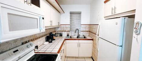A compact kitchen with white cabinets, a microwave, a stove, a sink, and a refrigerator.