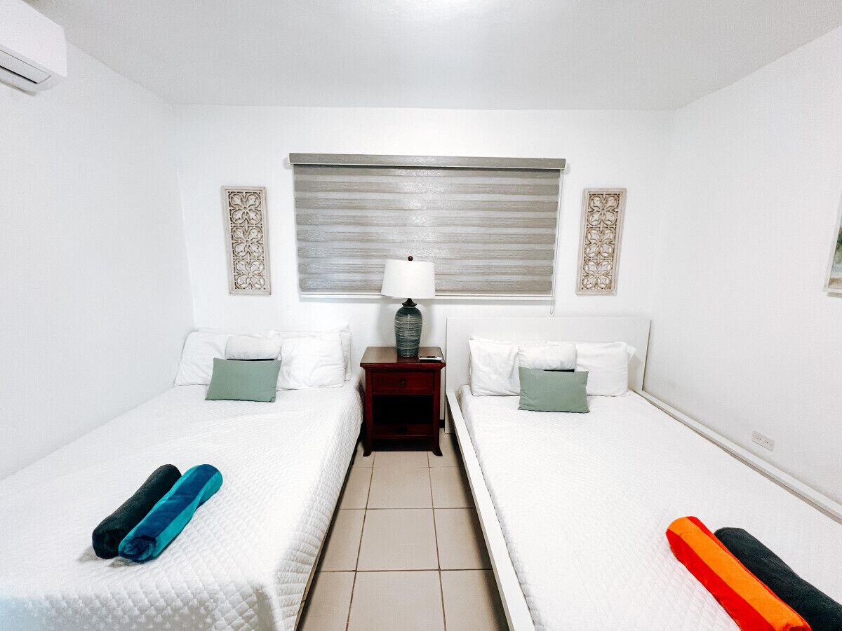 A hotel room with two single beds, a nightstand with a lamp, and decorative wall panels.