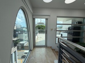 Un pasillo con una puerta de cristal que da a un balcón exterior con barandilla metálica.