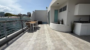 Une terrasse sur le toit avec une table et des chaises pour prendre les repas, un petit coin cuisine et une vue sur le panorama de la ville.