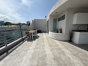 Une terrasse sur le toit avec une table et des chaises pour prendre les repas, un petit coin cuisine et une vue sur le panorama de la ville.