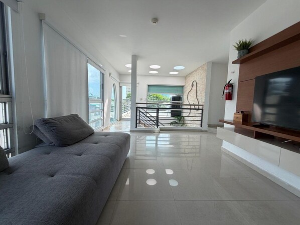 Una sala de estar moderna con un sofá gris, un televisor de pantalla plana sobre un mueble de madera y un balcón con vistas.