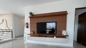 A modern living room with a flat-screen TV, wooden entertainment unit, and a fire extinguisher. - Elegant Modern PH W/ Balcony & Parking (San Juan)