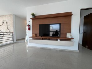 A modern living room with a flat-screen TV, wooden entertainment unit, and a fire extinguisher. - Elegant Modern PH W/ Balcony & Parking (San Juan)
