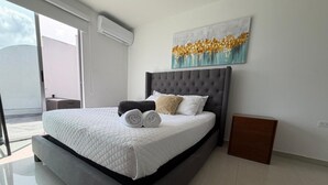 Une chambre moderne avec un grand lit, une tête de lit, une table de chevet, une commode, un climatiseur mural et une fenêtre donnant sur un beau paysage.
