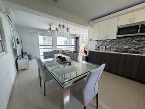 Una cocina moderna con una mesa de comedor de vidrio, armarios blancos y un microondas de acero inoxidable.