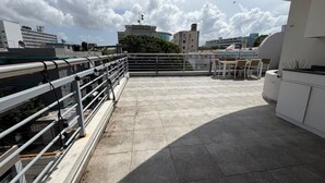 A rooftop terrace with a railing, a seating area, and a view of surrounding buildings. - Elegant Modern PH W/ Balcony & Parking (San Juan)