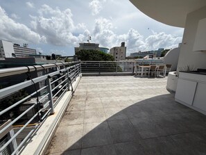 A rooftop terrace with a railing, a seating area, and a view of surrounding buildings. - Elegant Modern PH W/ Balcony & Parking (San Juan)