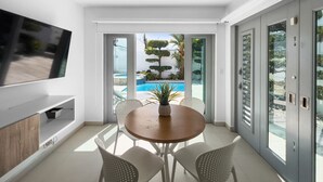 A modern living room with a flat-screen TV, a wooden dining table, and white chairs. - Spacious and Modern Villa with Pool in Ocean Park (San Juan)