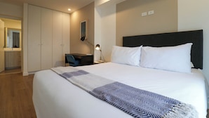 A hotel room with a large bed, a desk, a chair, and a wardrobe.