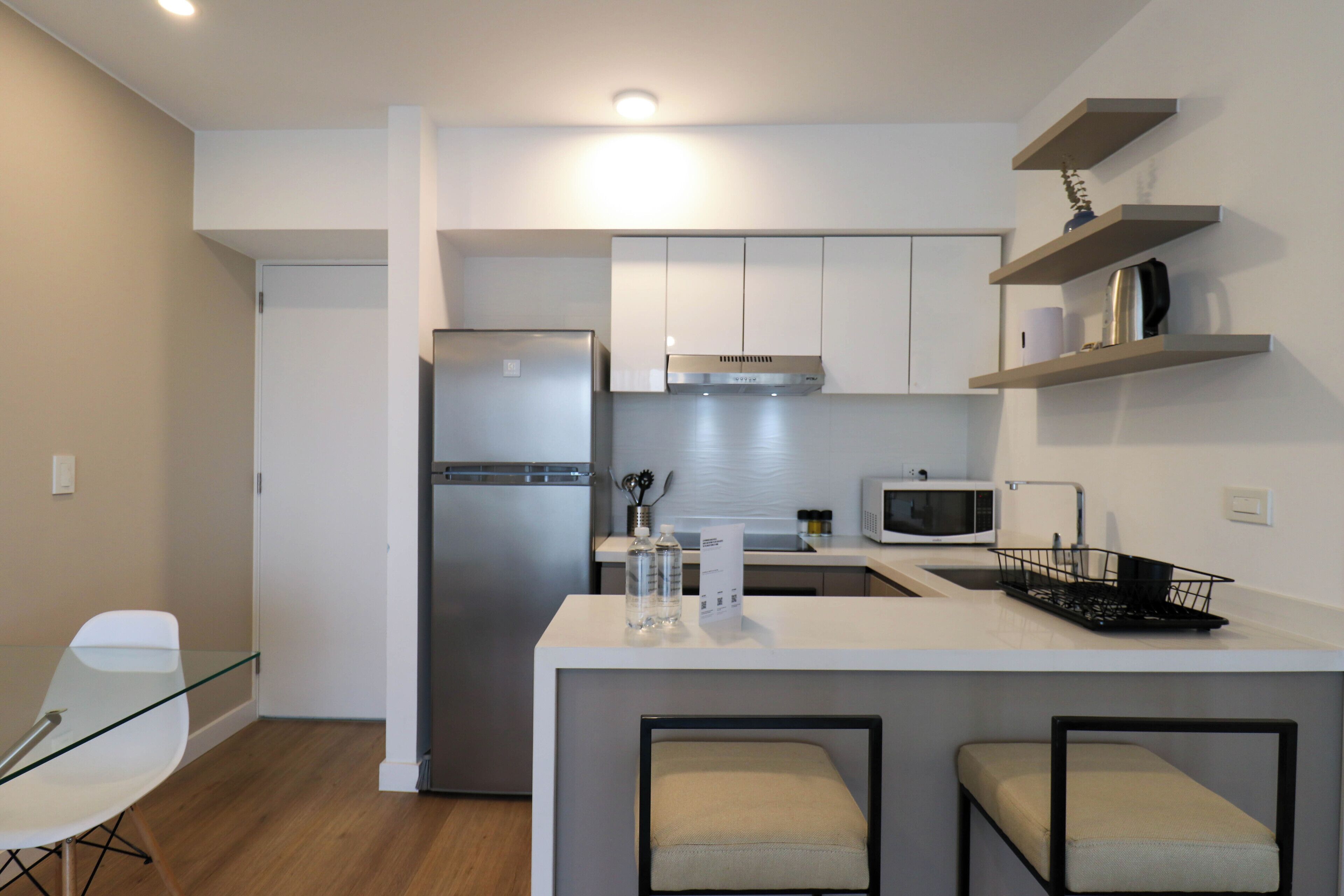 A modern kitchen with white cabinets, a stainless steel refrigerator, a microwave, and a small island with bar stools.