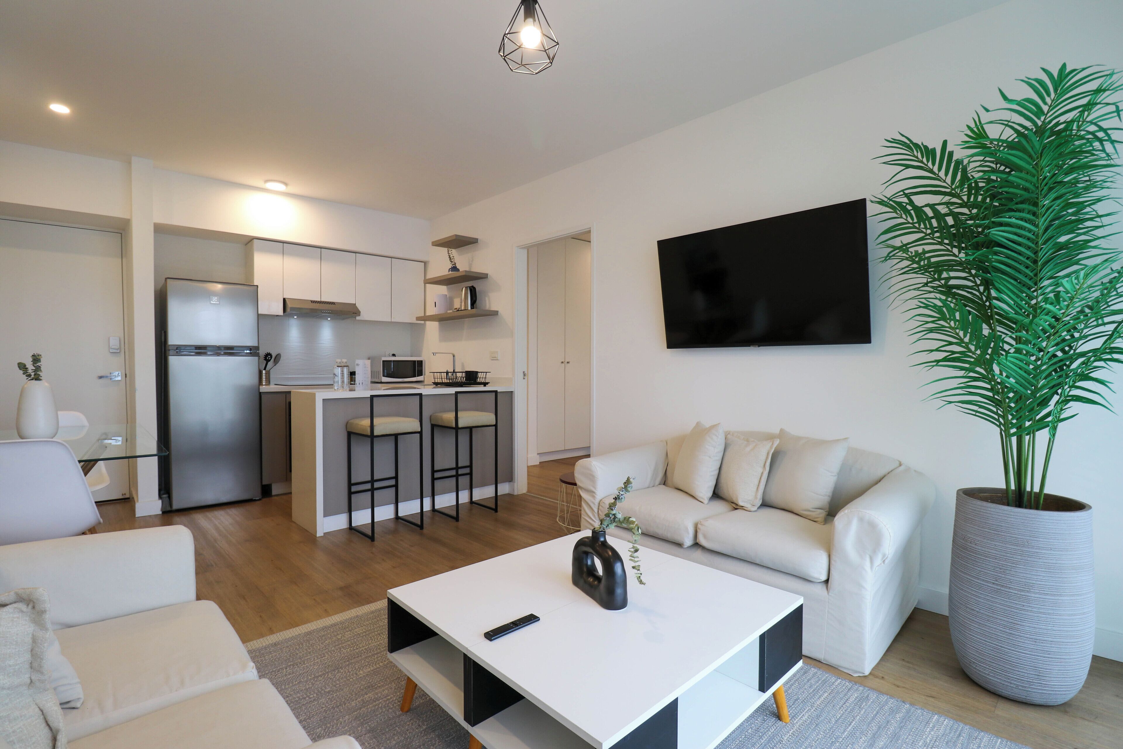 Een moderne woonkamer met een witte bank, een salontafel en een grote potplant.