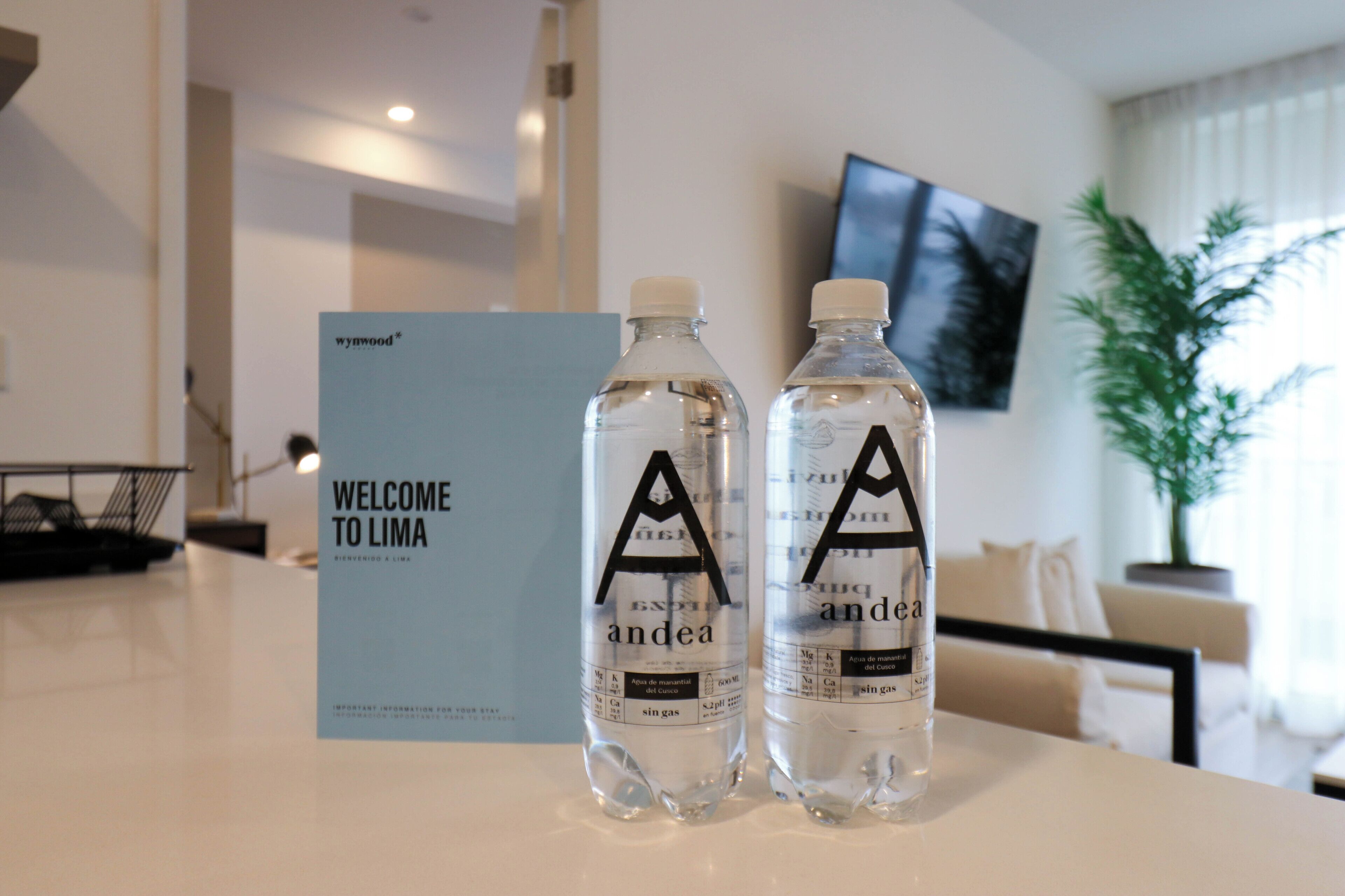 Two water bottles with labels on a table, a sign that reads "WELCOME TO LIMA," and a television mounted on the wall.
