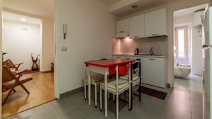 Una cucina compatta con mobili bianchi, un tavolo rosso e una lavatrice.