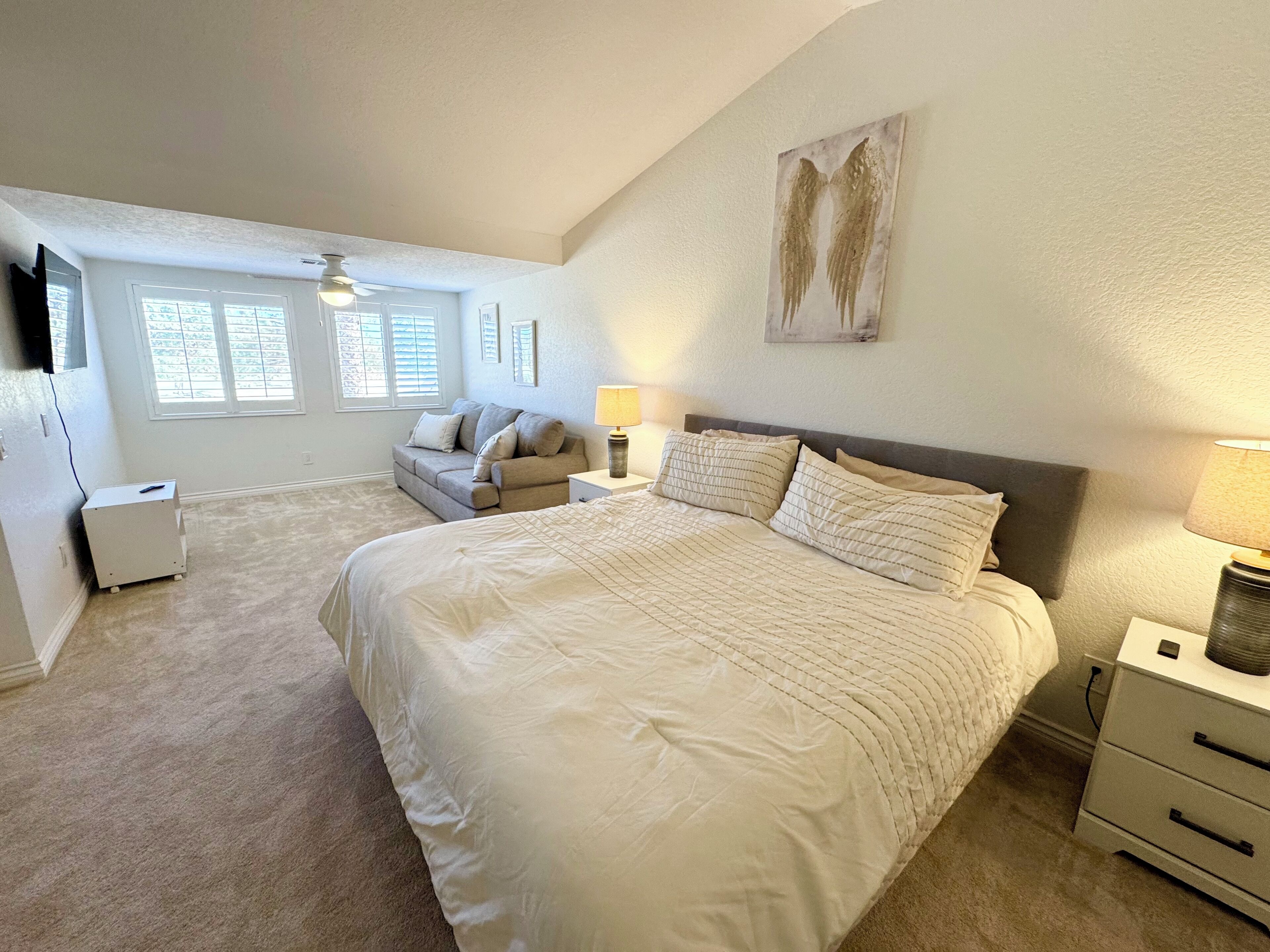 A bedroom with a large bed, a nightstand, a dresser, a sofa, and a ceiling fan.