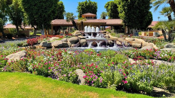 Un jardin agrémenté d’une fontaine, entouré de fleurs aux couleurs vives et de gros rochers.