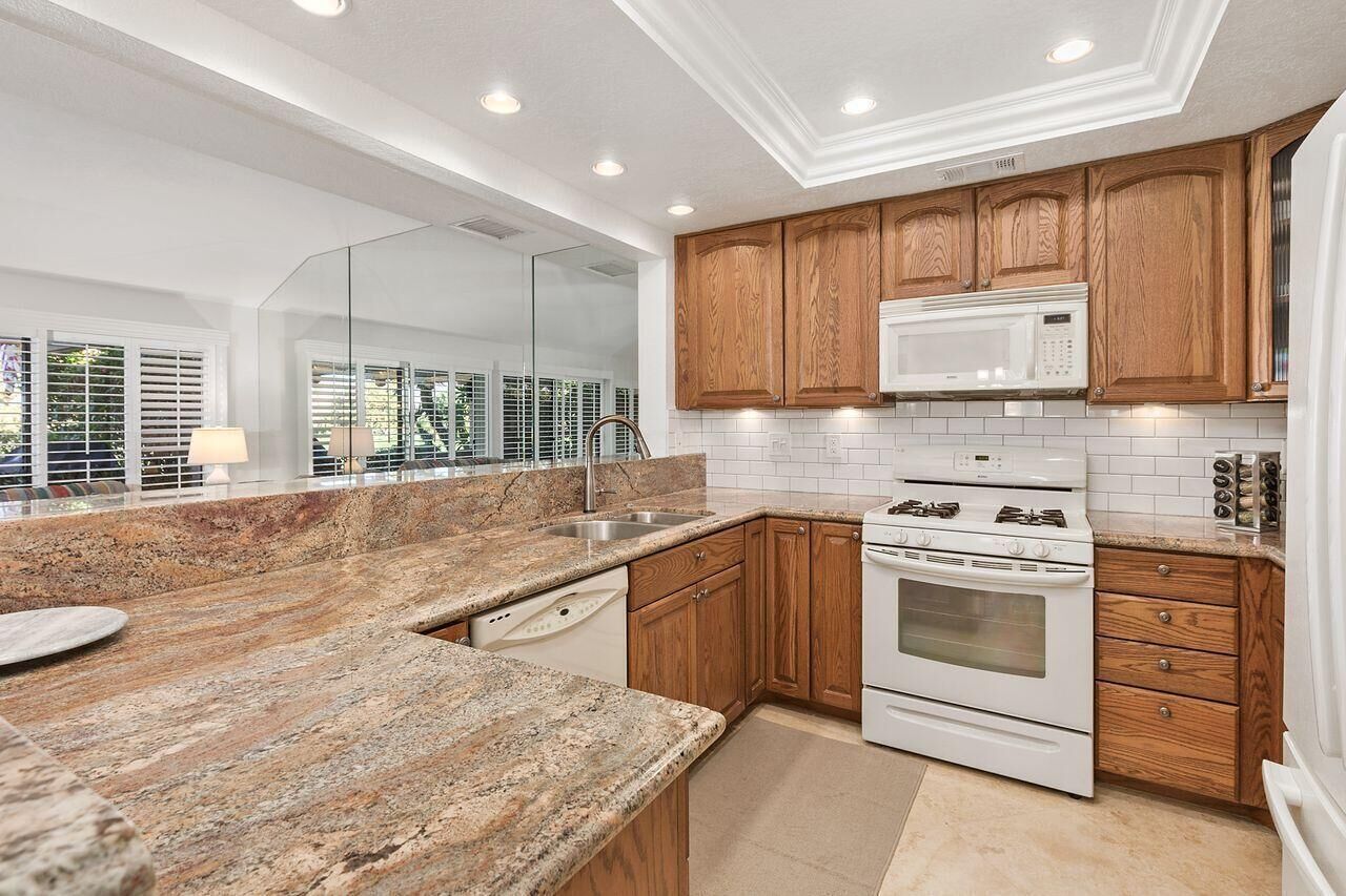 A modern kitchen with granite countertops, wooden cabinets, a built-in microwave, and a gas stove.