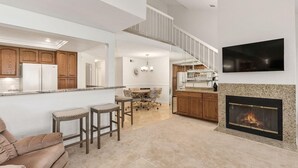 Un vaste espace de vie comprenant un coin salon avec cheminée, une table à manger et une cuisine à l’arrière-plan.