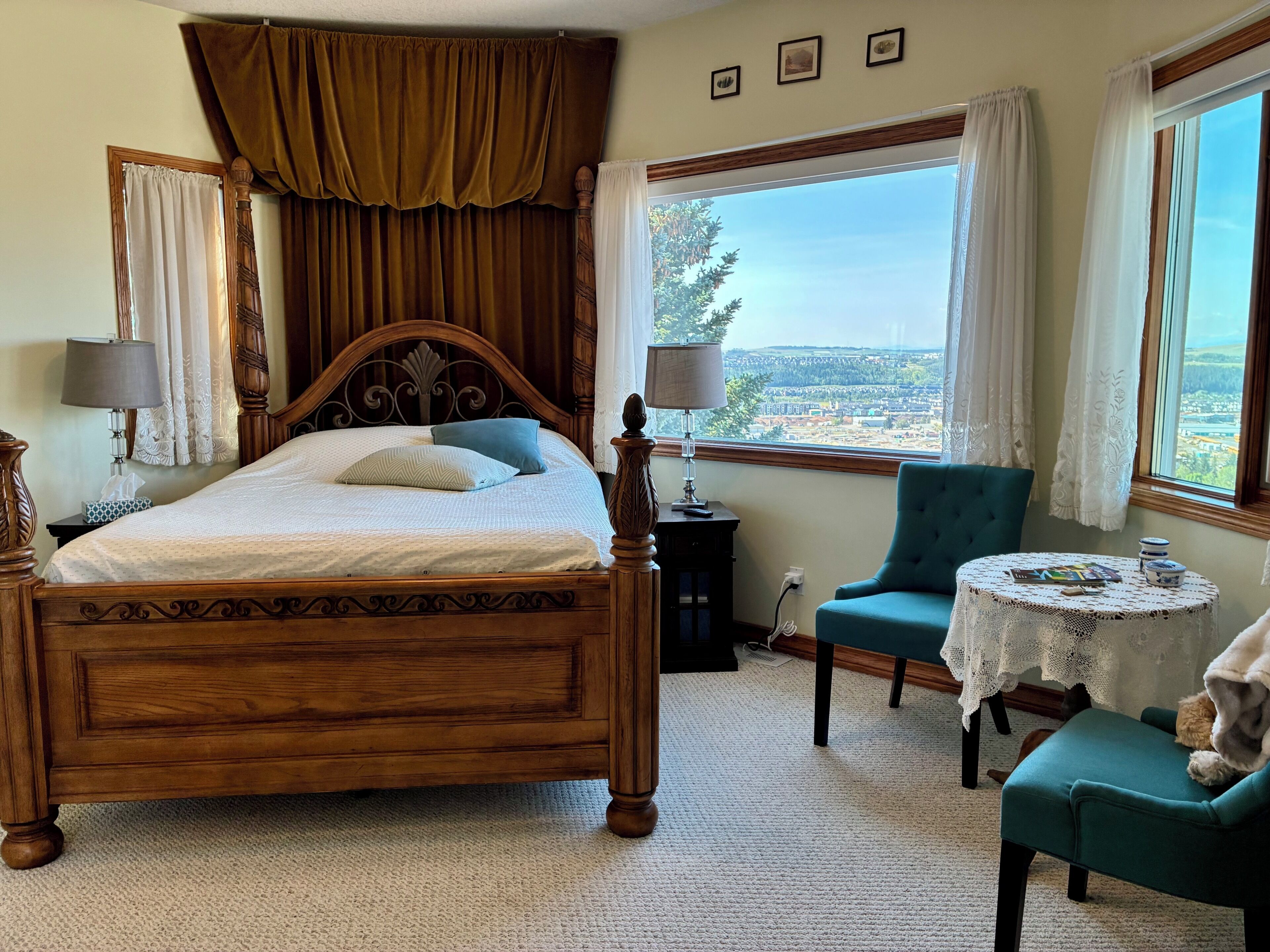 A bedroom with a large bed, a view of a landscape, a chair, and a small table.
