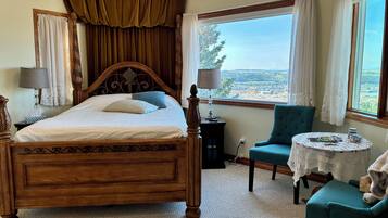 A bedroom with a large bed, a view of a landscape, a chair, and a small table.
