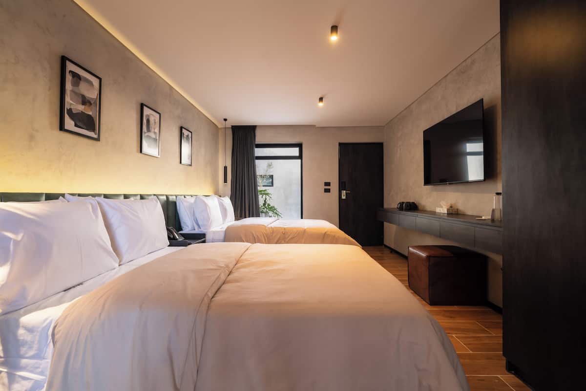 A hotel room with two beds, a flat-screen TV, a desk, and a large window.
